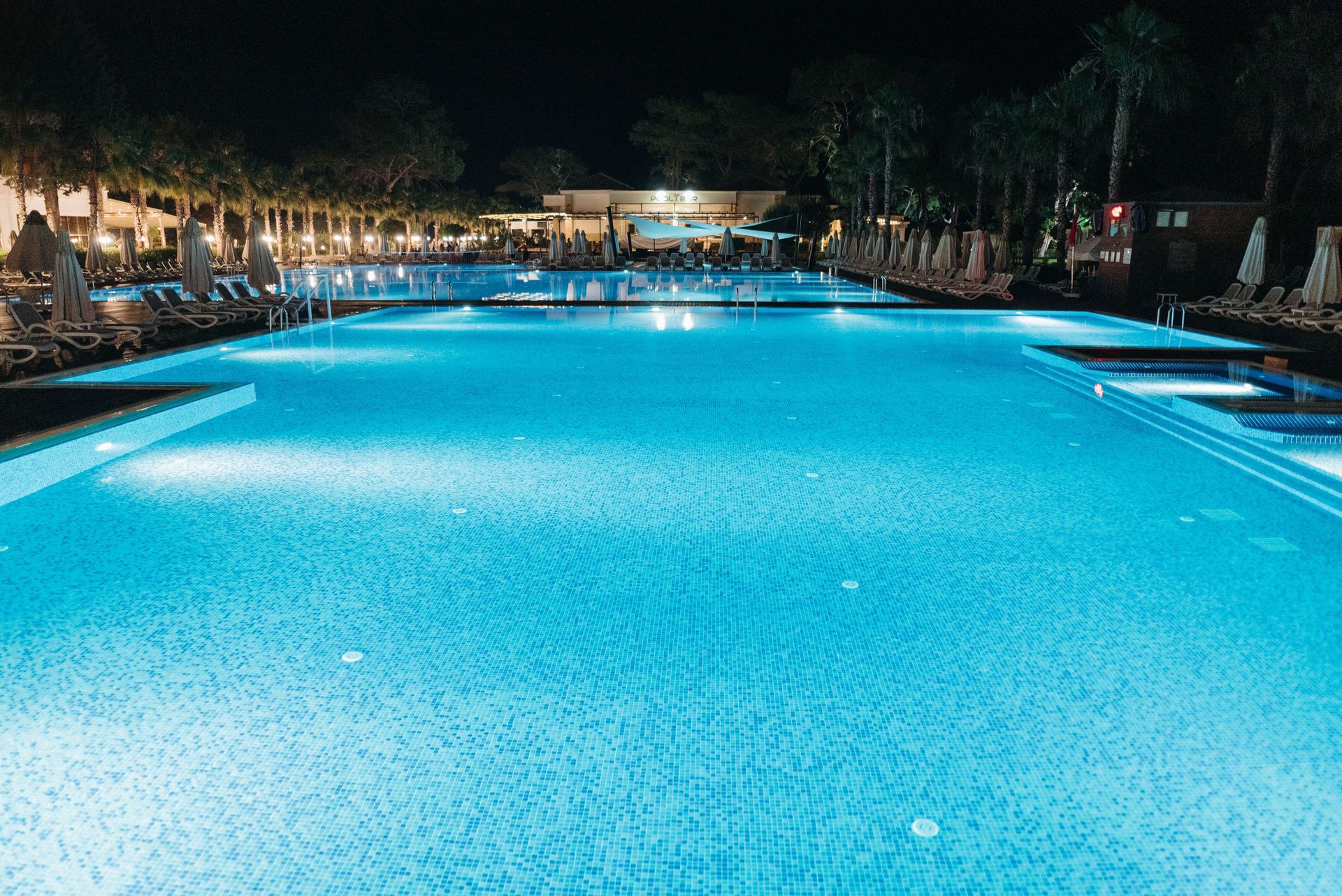 A luxurious resort swimming pool illuminated at night, offering a serene and elegant ambiance.